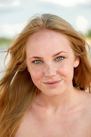 Freckled beauty shows her playful demeanor while stripping on a beach