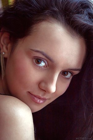 Curly-haired brunette takes off her see-through bodysuit on a bed