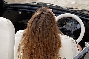 Dark-haired and baby-faced cutie posing naked in a luxurious car
