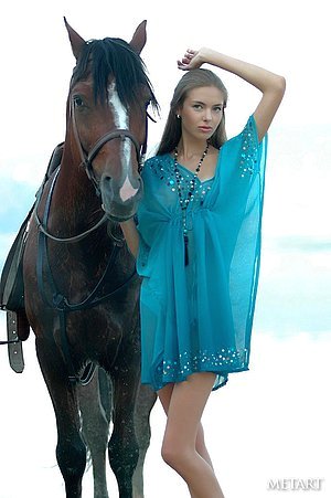 Horse girl posing next to a wild stallion in a outdoor erotic shoot